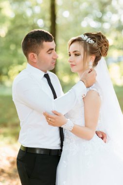 Bir adam ve bir kadın parkta birbirlerine sarılıyorlar. Adam kravat takıyor ve kadın beyaz bir elbise giyiyor. Sahne romantik ve mutlu.