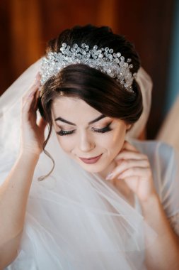 Beyaz peçeli ve başında taç olan bir kadın. Gülümsüyor ve kameraya bakıyor.