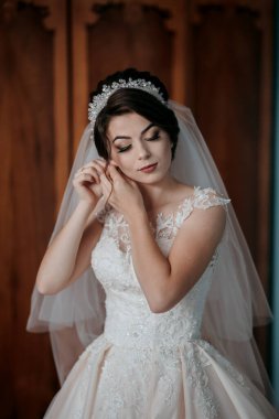 Gelinlik giymiş bir kadın aynada kendine bakıyor. Bir taç ve duvak takıyor.