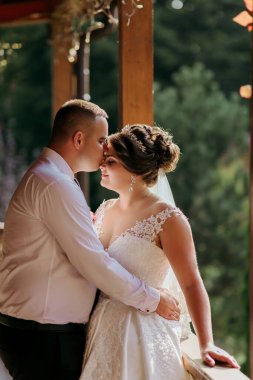 Bir gelin ve damat birbirlerini yanağından öpüyor. Gelin beyaz bir elbise giyiyor ve damat beyaz bir gömlek giyiyor.