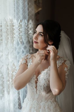 Bir kadın düğünü için hazırlanıyor ve duvağını takıyor. Pencereden dışarı bakıyor, muhtemelen manzaraya hayran ya da birini bekliyor.