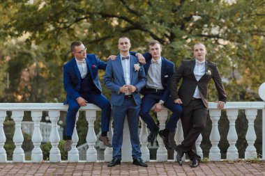 Takım elbiseli bir grup adam korkulukta fotoğraf çektirmek için poz veriyor. Erkekler takım elbise ve kravat giydiği için sahne resmi ve profesyonel. Fotoğrafın ayarları bir köprü.