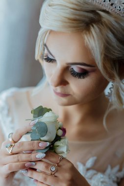 Bir kadın elinde beyaz bir gül tutuyor. Taç takıyor ve saçları topuz şeklinde.