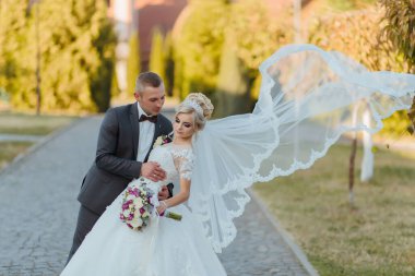 Gelin ve damat, beyaz bir duvak takan gelinle tuğladan bir geçitte duruyorlar.