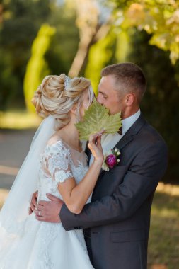 Bir gelin ve damat bir yaprağa sarılıp öpüşüyorlar. Sahne romantik ve samimi.
