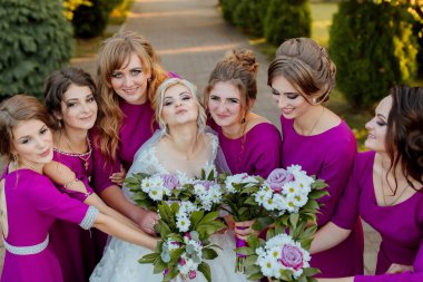 Pembe elbiseli bir grup kadın resim için poz veriyor. Kadınlardan biri elinde bir buket çiçek tutuyor.