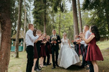 Bir gelin ve damat düğün partileri arkalarında bir patikada yürüyorlar. Gelin beyaz bir elbise giyiyor ve damat bir takım elbise giyiyor. Düğün grubu siyah ve kırmızı giyinmiş.