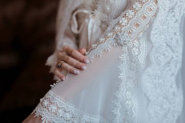 Beyaz dantelli bir elbise giyen ve kolunu tutan bir kadın. Elbise beyaz ve dantelli.