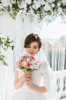 Bir gelin elinde pembe ve beyaz çiçeklerden bir buket tutuyor. Beyaz bir elbise ve duvak takıyor. Sahne bir bahçede ya da bir düğün salonunda geçiyor.