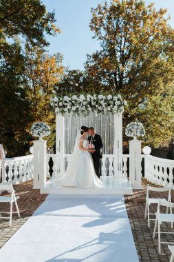 Bir gelin ve damat kemer yolunun önünde beyaz bir halı ile kemer yoluna doğru ilerliyorlar.