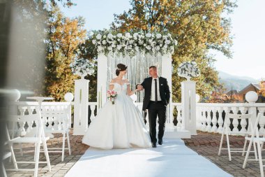 Bir gelin ve damat üzerinde beyaz bir kemerle beyaz bir koridorda yürüyorlar. Gelin beyaz bir elbise giyiyor ve damat siyah bir takım elbise giyiyor. Sahne bir bahçede ya da dışarıda geçiyor.