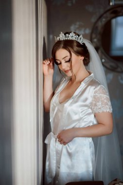 Kafasında taç olan beyaz elbiseli bir kadın. Duvara yaslanıyor.