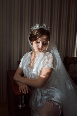 Beyaz bir elbise ve taç giyen bir kadın kanepede oturur. Gülümsüyor ve kameraya bakıyor.