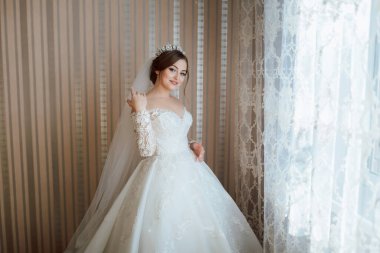 Gelinlikli bir kadın pencerenin önünde duruyor. Duvak ve taç takıyor.