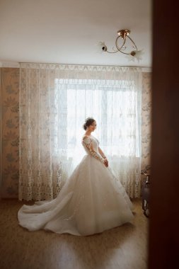 Beyaz elbiseli bir kadın pencerenin önünde duruyor. O bir taç takıyor ve pencereden dışarı bakıyor.