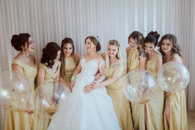 Bir grup kadın fotoğraf için poz veriyor, içlerinden biri gelinlik giyiyor. Hepsinin elinde balonlar var ve görüntünün havası neşeli ve kutlayıcı.