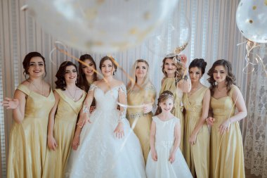 Sarı elbiseli bir grup kadın fotoğraf için poz veriyor. Kadınlardan biri balon tutuyor.