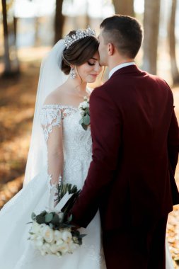 Bir gelin ve damat ormanda sarılıp öpüşüyorlar. Gelin beyaz bir elbise ve taç giyiyor.