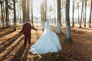 Bir gelin ve damat el ele bir ormanda yürüyorlar. Gelin uzun beyaz bir elbise giyiyor ve damat kırmızı bir takım elbise giyiyor. Sahne huzurlu ve romantik.