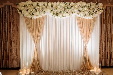 Üzerinde çiçekler olan altın ve beyaz bir perde. Perde duvardan sarkıyor.