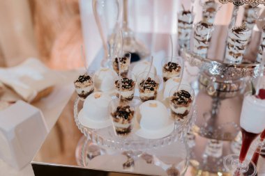 Kekler ve diğer ikramlar da dahil olmak üzere çeşitli tatlıların yer aldığı bir masa cam bir kabın içinde sergileniyor. Tatlılar küçük bardaklarda sıralanır ve kaşıklarla kaplanır. Bu da servis edilmelerini kolaylaştırır.