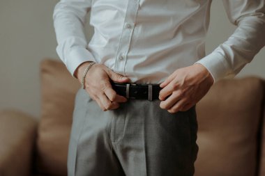 Beyaz gömlekli bir adam kemerini ayarlıyor. Formalite kavramı ve detaylara dikkat