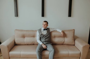 Takım elbiseli ve papyonlu bir adam kanepede oturur. Kanepe açık pembe bir renktir.