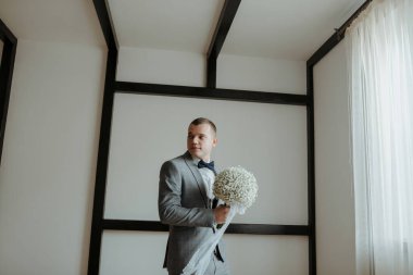 Takım elbiseli bir adam elinde bir buket beyaz çiçek tutuyor. Zarafet ve entelektüellik kavramı. Çünkü adam takım elbise ve kravat takmış.