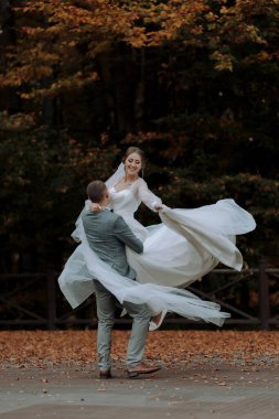 Bir adam ve bir kadın sonbaharda dans ediyorlar. Adam kadının elini tutuyor ve ikisi de gülümsüyor.