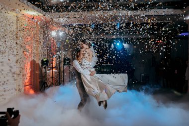 Bir çift havada dans ediyor ve etraflarına konfeti dökülüyor. Sahne neşeli ve kutlayıcıdır.