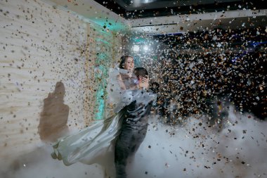 Bir çift havada dans ediyor ve etraflarına konfeti dökülüyor. Sahne kutlama ve neşe dolu.