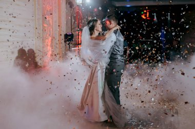 Bir gelin ve damat etraflarında konfeti düşerken havada dans ediyorlar. Sahne neşeli ve kutlayıcıdır.