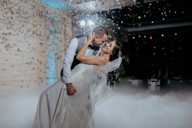 Bir gelin ve damat etraflarında konfeti düşerken havada dans ediyorlar. Sahne neşeli ve kutlayıcıdır.