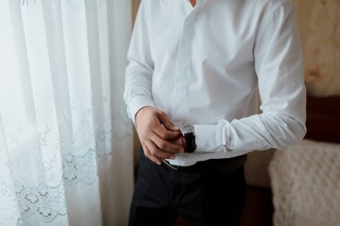 Beyaz gömlekli ve siyah pantolonlu bir adam saat takıyor ve gömleğini düzeltiyor. Formalite anlayışı ve detaylara dikkat, adam görünüşünün düzgün ve parlak olduğundan emin olmak için özen gösteriyor.