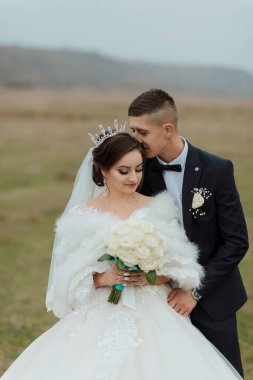 Gelin ve damat bir tarlada, gelinle birlikte beyaz kürk şort ve taç giyiyorlar.