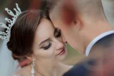 Bir gelin ve damat birbirlerinin dudaklarını öpüyor. Gelin taç takıyor ve damat da takım elbise giyiyor.