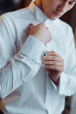 Bir adam beyaz bir gömlek giyiyor ve elmas bir kol düğmesi takıyor. Adam takım elbise ve kravat giydiği için resmiyet ve zarafet kavramı.