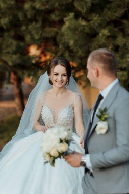 Gelin ve damat bir ağacın önünde, gelin bir buket tutuyor.