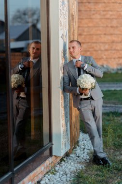 Takım elbiseli bir adam elinde bir buket beyaz çiçekle pencerenin önünde duruyor.