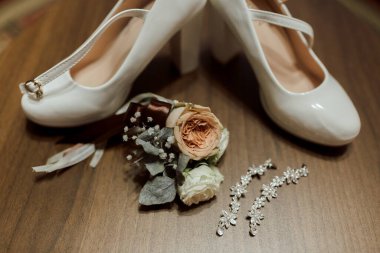 Üzerinde çiçek olan beyaz bir çift ayakkabıya. Ayakkabılar ahşap bir masaya konur.