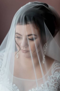 Bir kadın yüzünü kısmen kapatan bir peçe takıyor. Çok güzel bir gülümsemesi var ve gözleri kapalı. Duvak beyaz ve dantel bir tasarımı var.