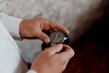 Bir adam bir saat tutuyor ve ona bakıyor. Saat siyah ve gümüş bir şeridi var.