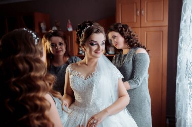 Bir gelin nedimeleriyle düğününe hazırlanıyor. Gelin beyaz bir elbise ve duvak takıyor.
