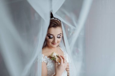 Bir gelin elinde çiçekle bir resim için poz veriyor. Resmin romantik ve zarif bir havası var, gelin beyaz bir elbise giymiş ve elinde bir gül tutuyor.