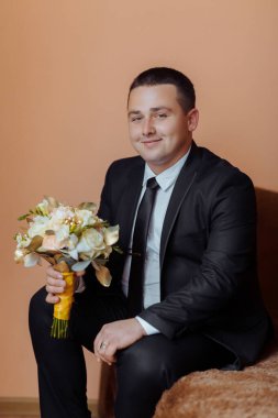 Takım elbiseli ve kravatlı bir adam bir buket çiçekle kanepede oturuyor. Zarafet ve entelektüellik anlayışı, çünkü adam resmi giyinmiş.