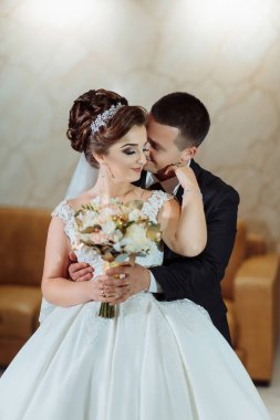 Bir gelin ve damat bir buket tutarken birbirlerine sarılıp öpüşüyorlar. Gelin beyaz bir elbise giyiyor ve damat bir takım elbise giyiyor. Sahne romantik ve mutlu.
