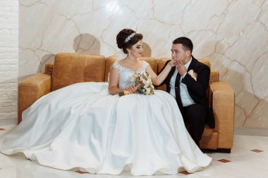 Gelin ve damat bir kanepede oturuyor, gelin bir buket tutuyor. Sahne romantik ve samimi.