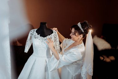 Bir kadın düğünü için hazırlanıyor ve bir elbisenin dantelini ayarlıyor. Elbise beyaz ve dantel yakalı.