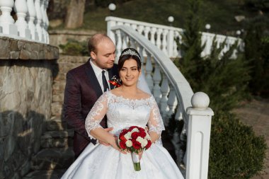 Gelin ve damat bir merdivende duruyorlar, gelin elinde bir buket kırmızı çiçek tutuyor.
