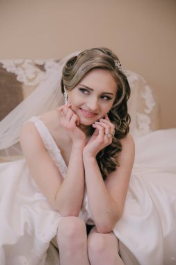 Bir gelin elleri dizlerinin üzerinde bir yatakta oturuyor. Beyaz bir elbise ve duvak takıyor.